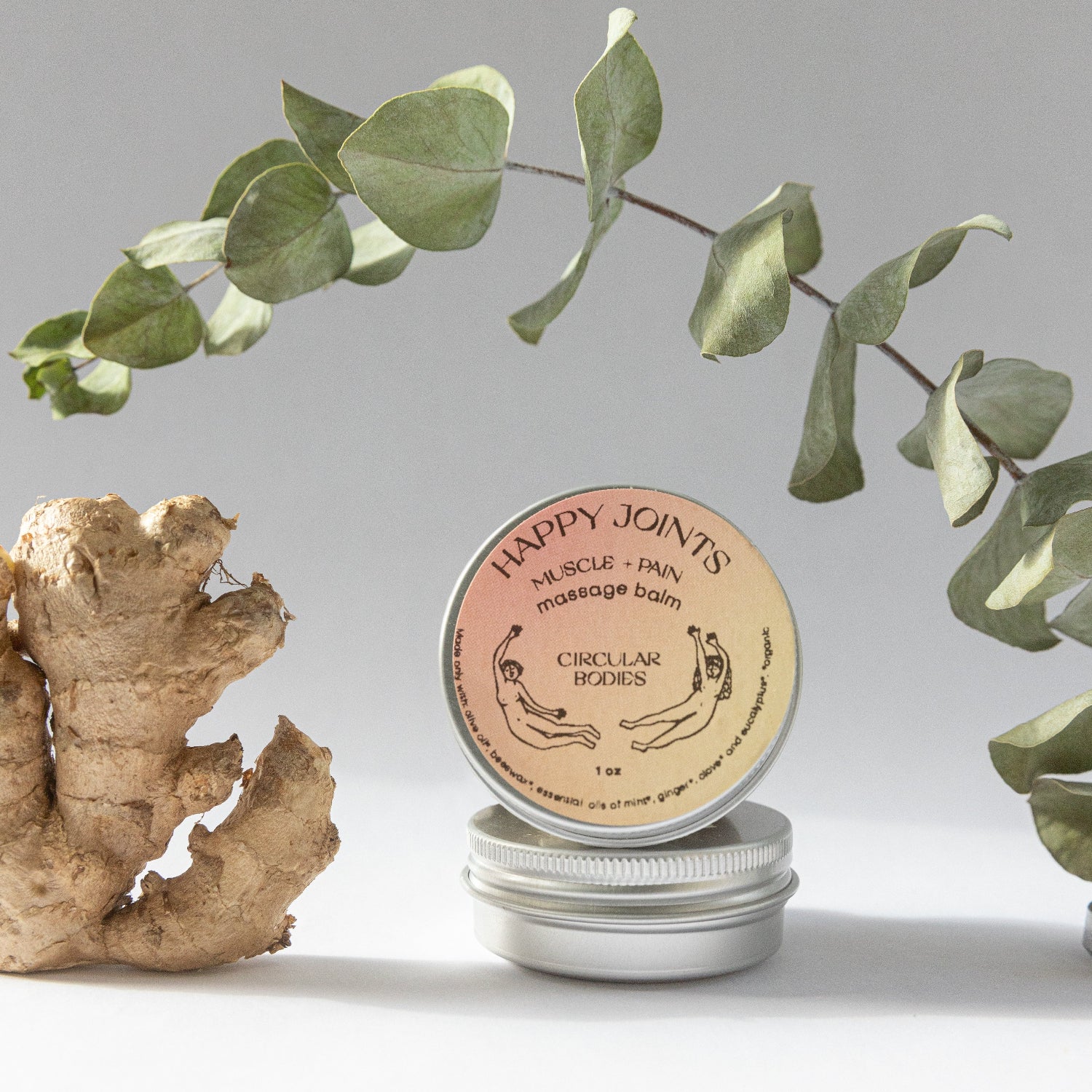 Round container labeled 'Happy Joints' with a ginger root and eucalyptus leaves on a light background