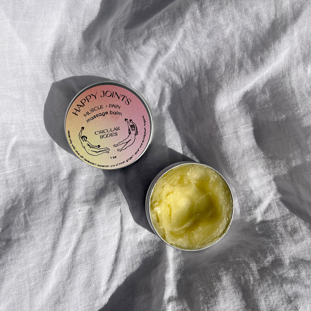 Container of 'Happy Joints' massage balm on a textured fabric background