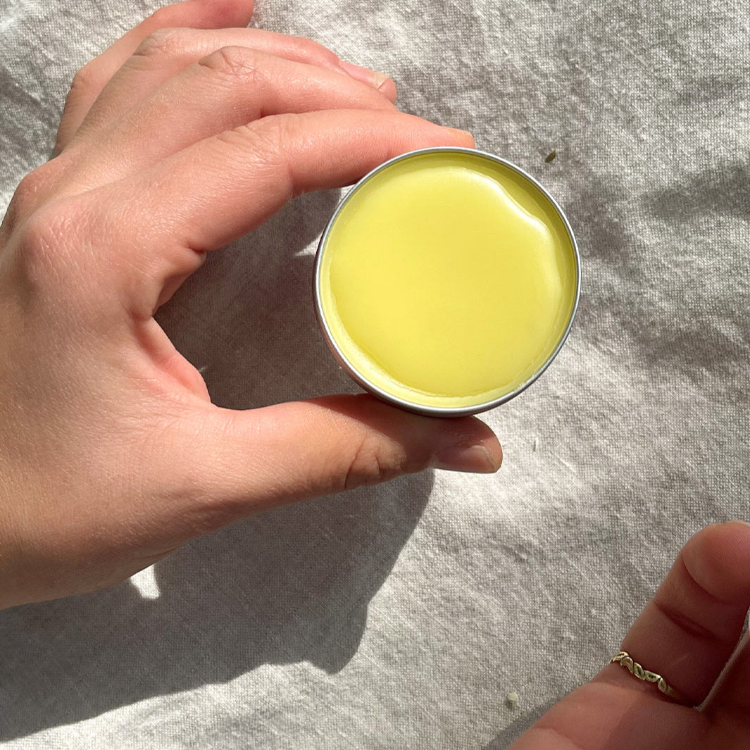 Hand holding a small container of yellow cream against a textured gray background